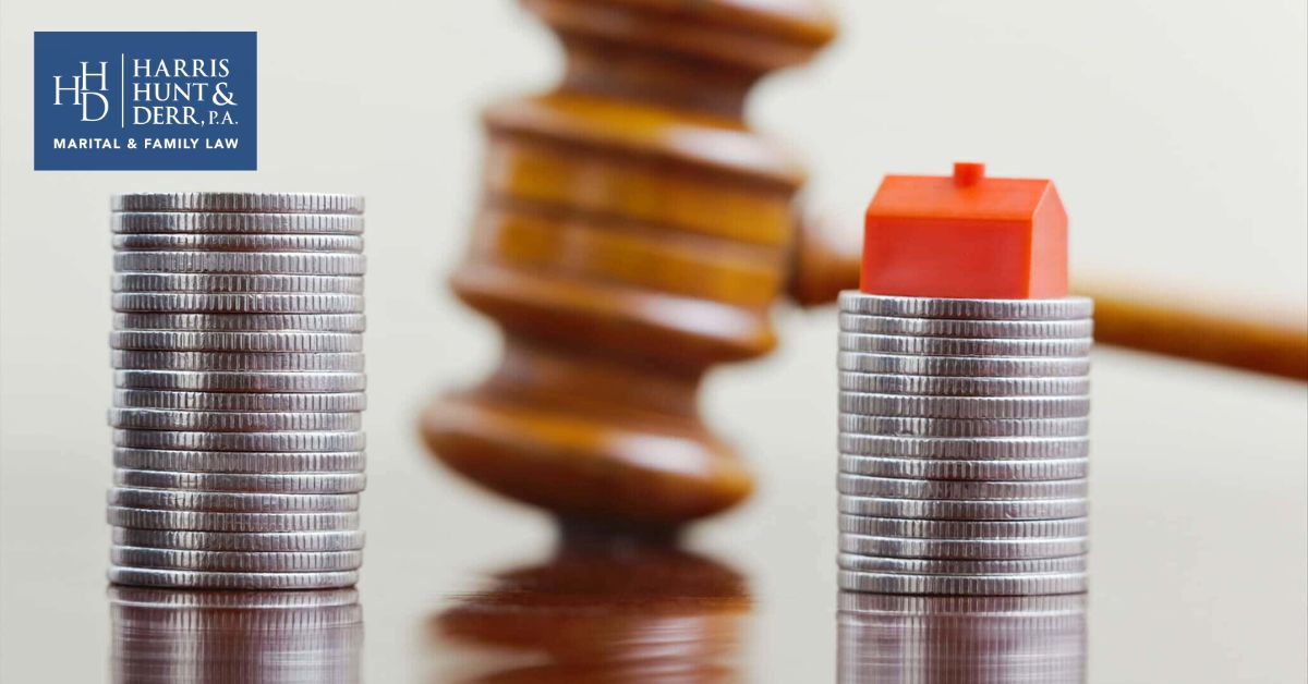 A gavel and stacks of coins with a small red house, symbolizing property division in a legal context. HARRIS HUNT & DERR, P.A. MARITAL & FAMILY LAW.